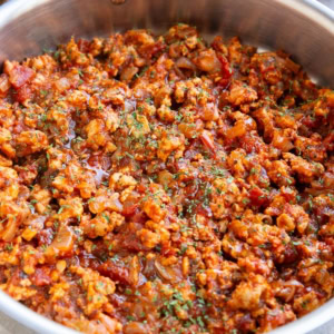 Large stainless steel skillet full of turkey bolognese sauce with fresh parsley to the side and dried parsley sprinkled on top.