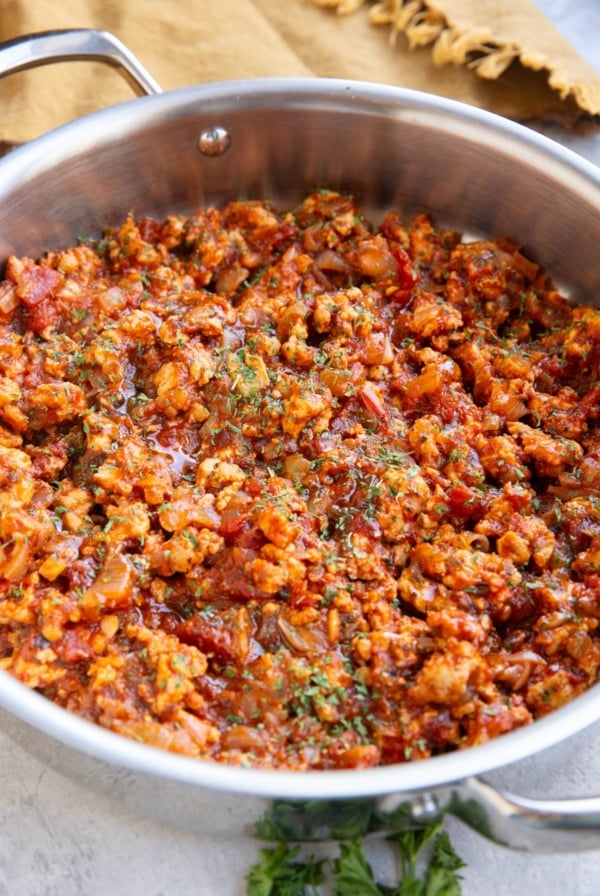 Large stainless steel skillet full of turkey bolognese sauce with fresh parsley to the side and dried parsley sprinkled on top.