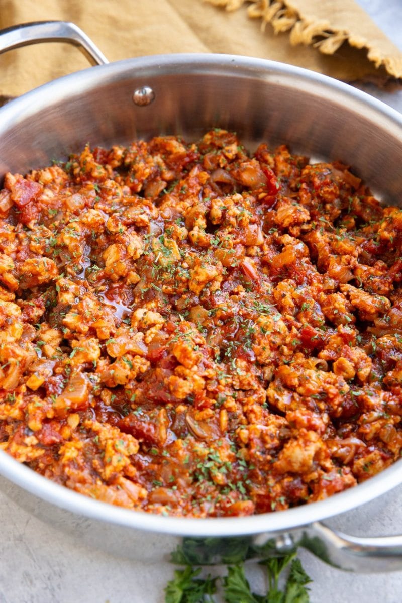 Large stainless steel skillet full of turkey bolognese sauce with fresh parsley to the side and dried parsley sprinkled on top.