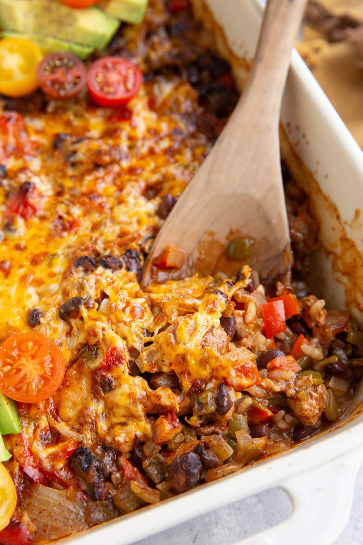 Casserole dish full of cheesy chicken taco casserole with a wooden spoon to the side.