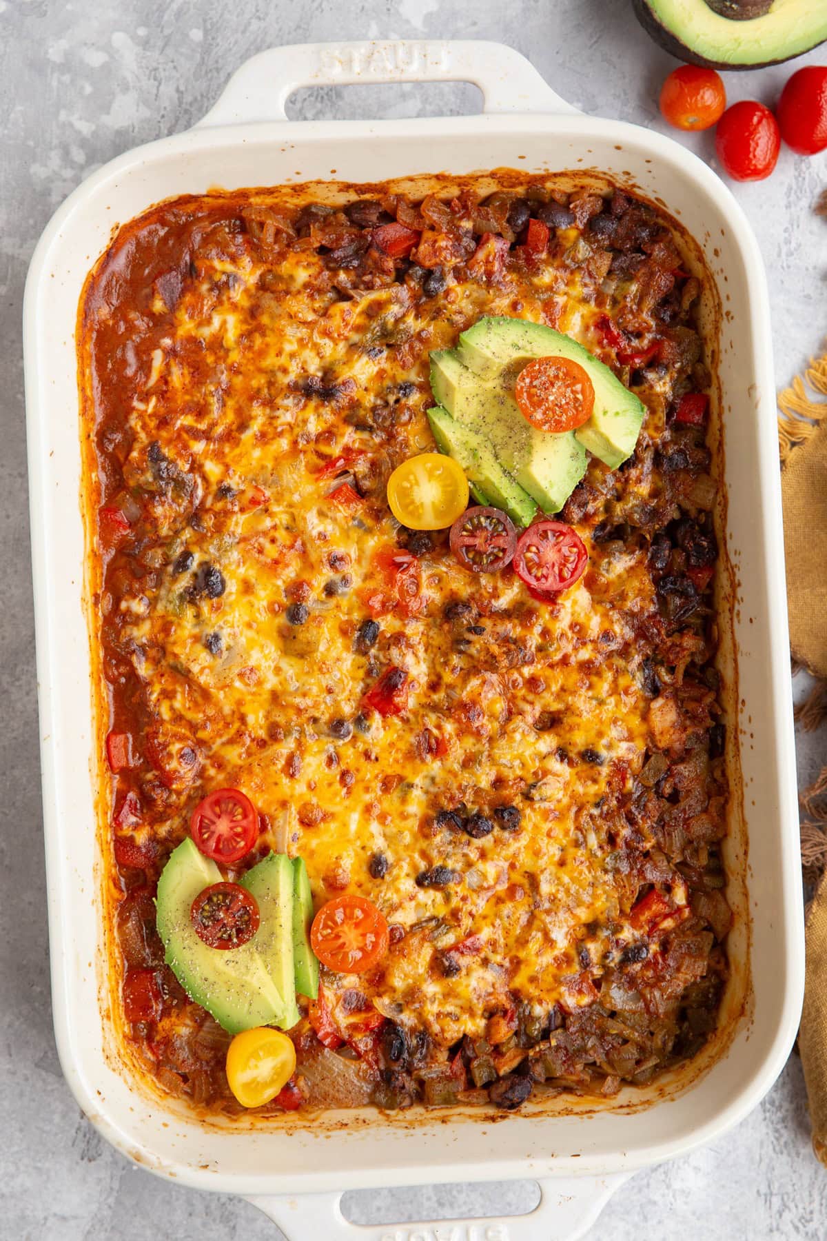 Large casserole dish of chicken taco casserole topped with sliced avocados and chopped cherry tomatoes. Ready to serve.