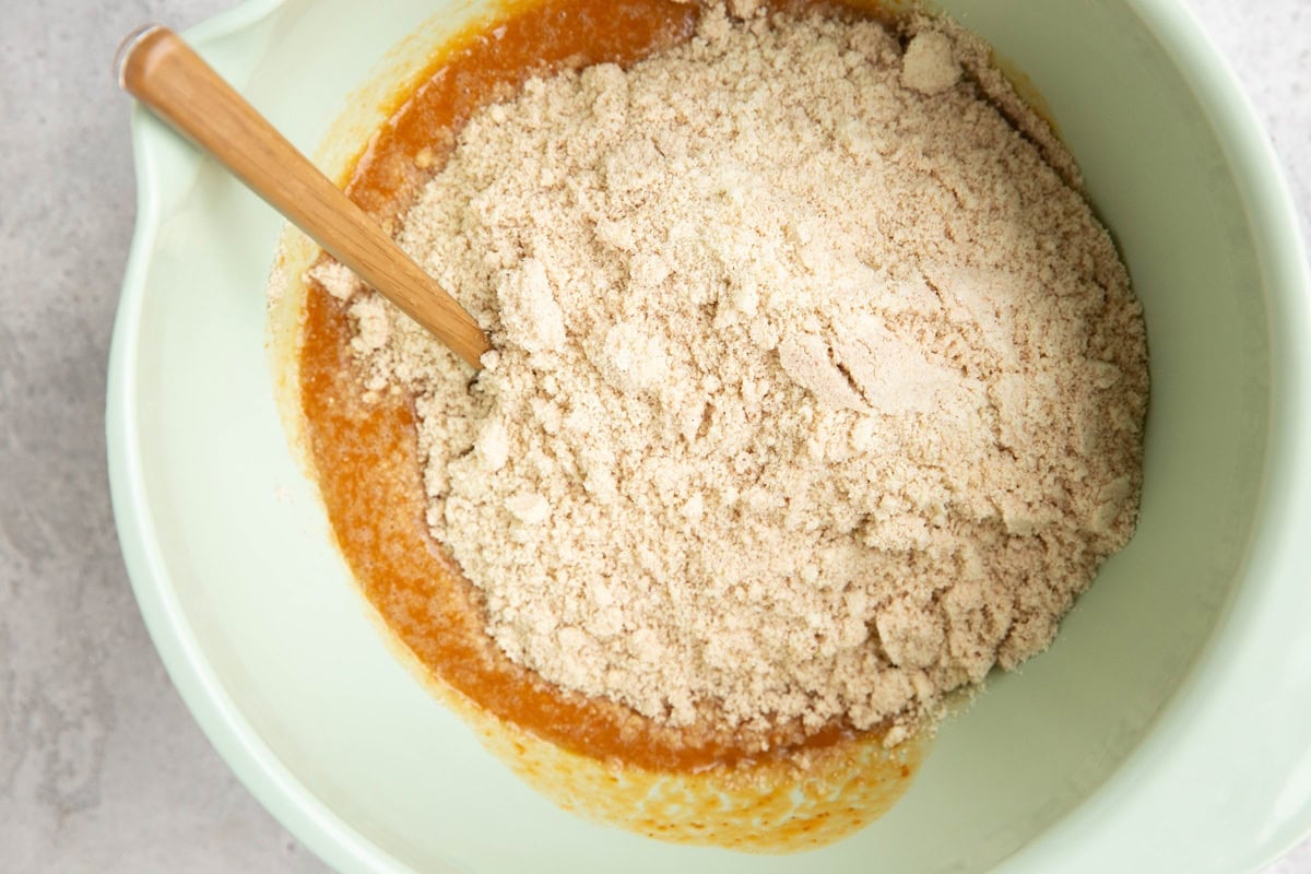 Mixing bowl with pumpkin mixture on the bottom and almond flour mixture on top, ready to be mixed in.
