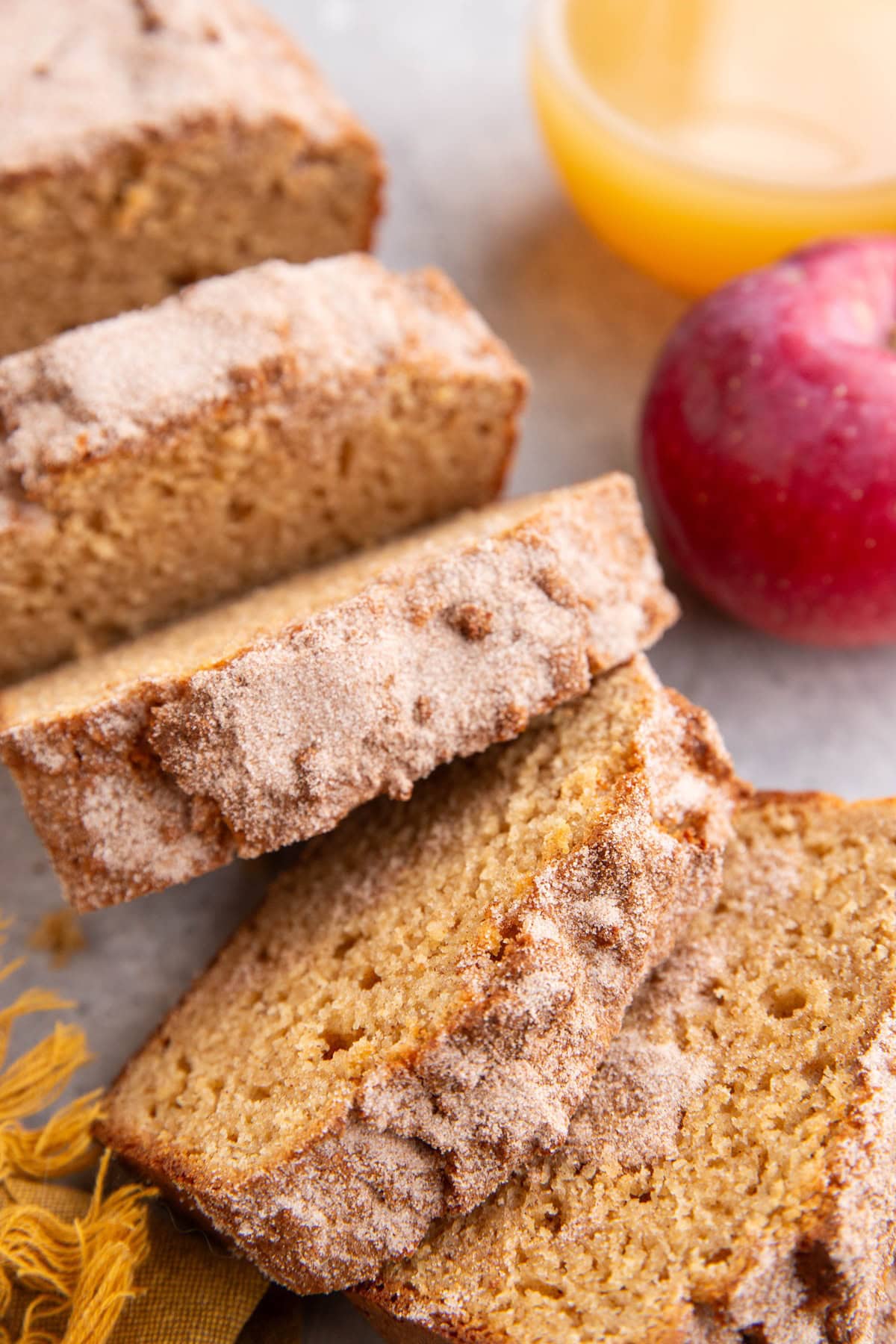Apple cider donut bread cut into slices with apple cider in a glass and a fresh apple in the background.