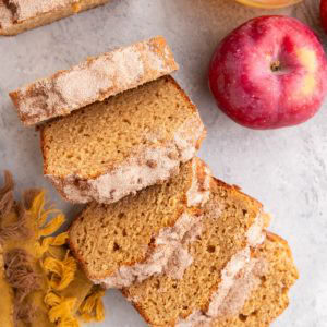 Loaf of apple cider bread cut into slices with a fresh apple and a glass of apple cider to the side.
