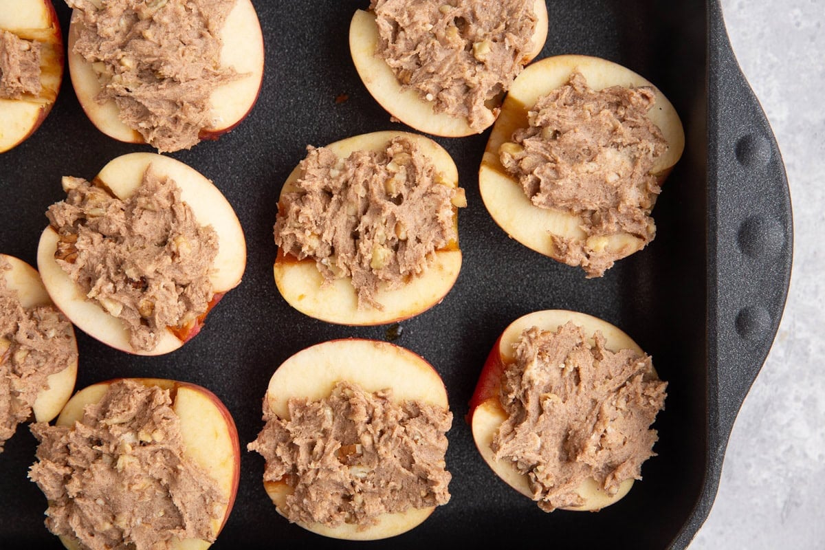 Baking dish full of halved apples stuffed with cobbler topping mixture, ready to go into the oven.