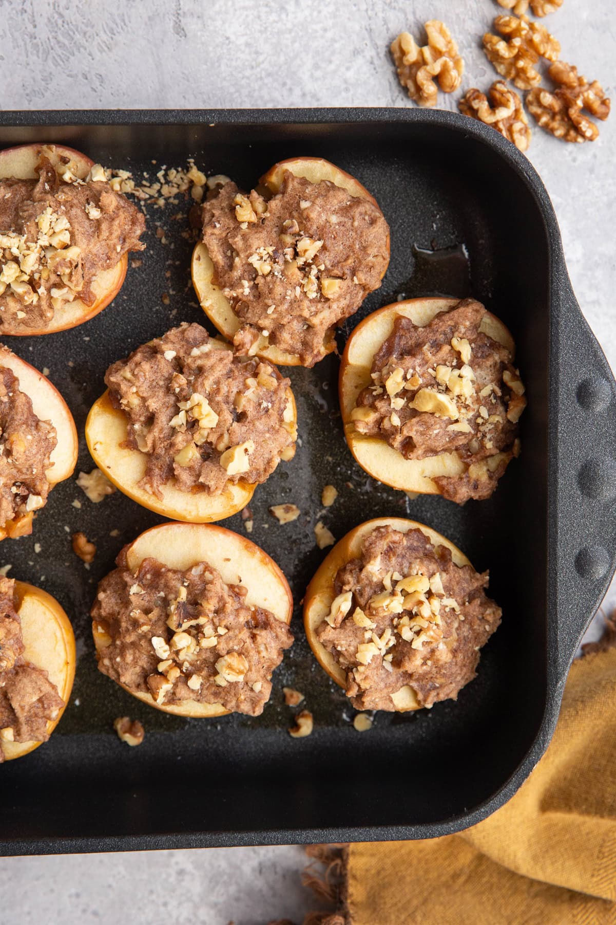 Large baking dish with baked apples stuffed with cobbler filling and chopped walnuts, fresh out of the oven with raw walnuts to the side.