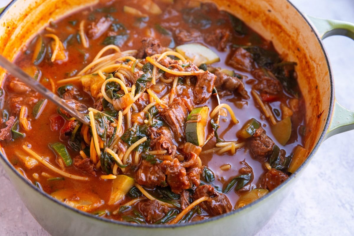 Large pot of birria soup with noodles and fresh vegetables.