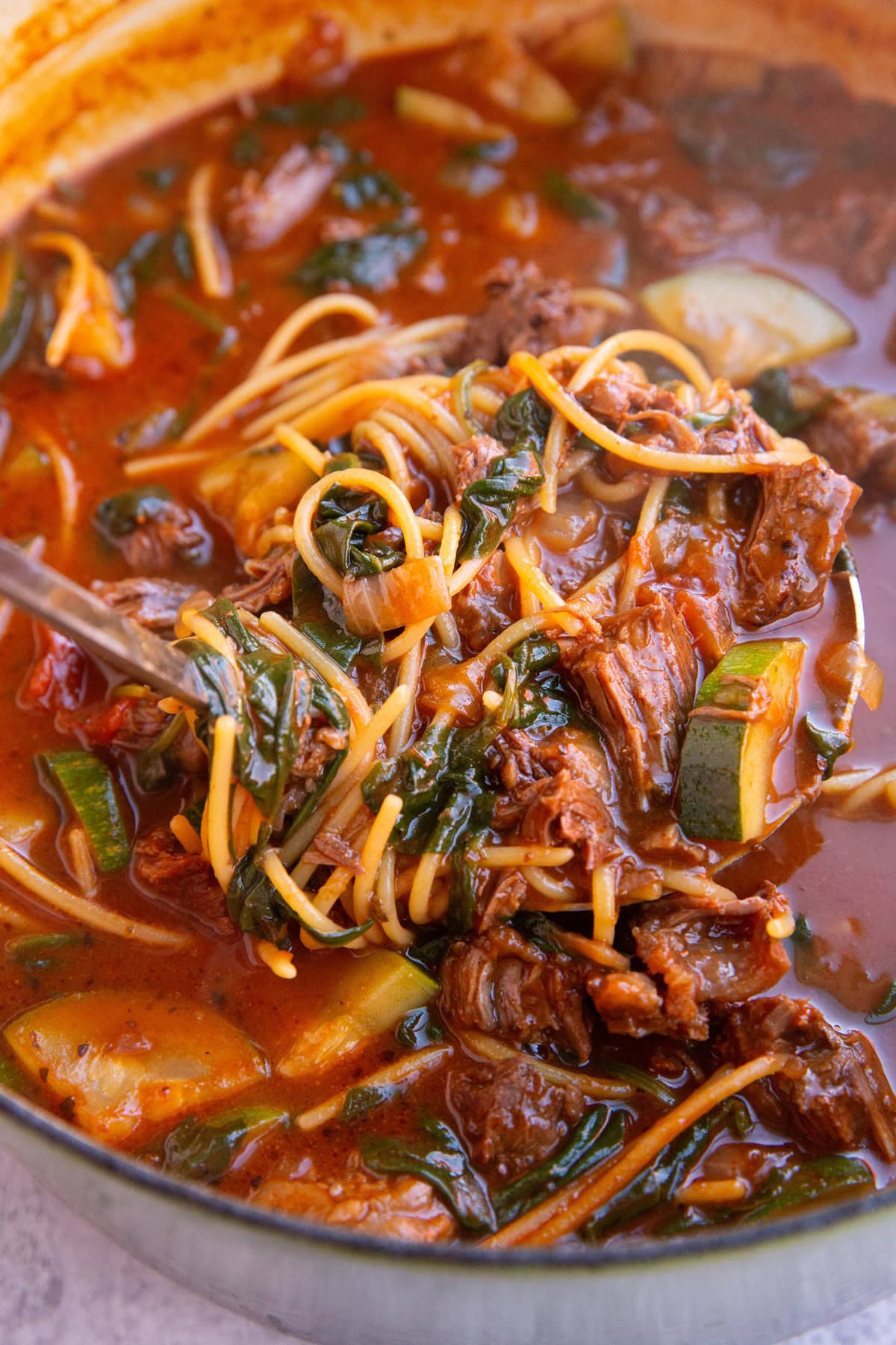 Large pot of birria soup with noodles and vegetables and a ladle taking a scoop out to serve.