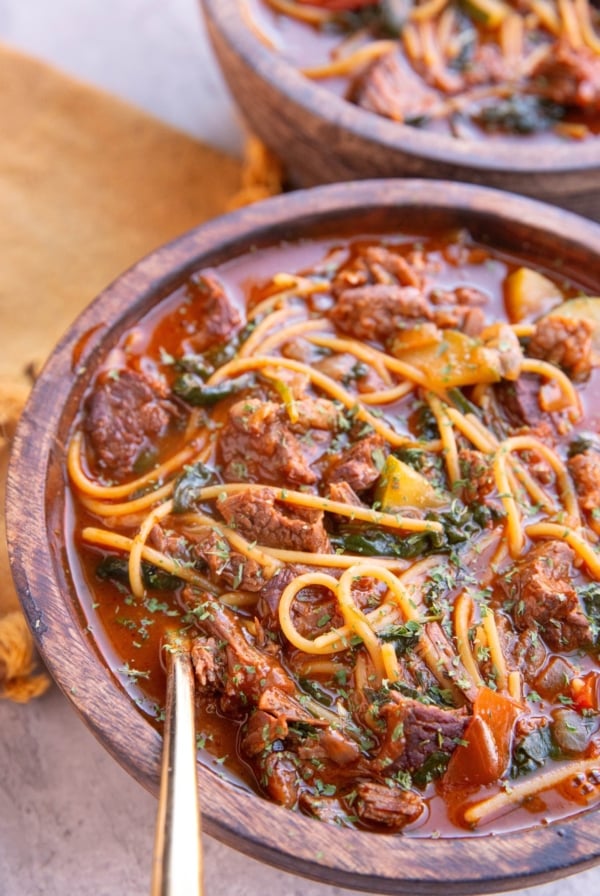 Two bowls of birria soup in wooden bowls with a golden spoon, ready to serve.