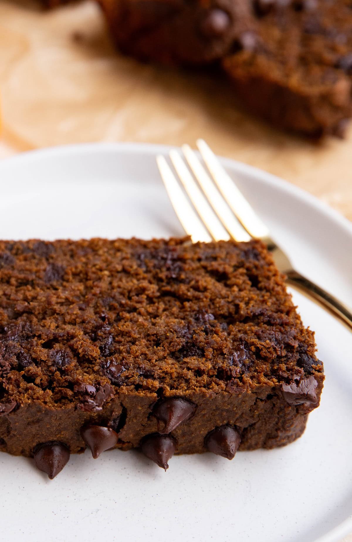 Slice of chocolate sweet potato bread on a plate with the rest of the loaf sliced in the background.