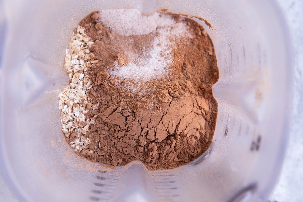 Blender with oats, cocoa powder, salt, cinnamon, and baking powder inside.