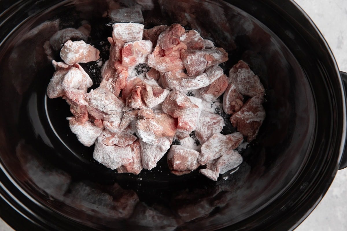 Flour coated beef at the bottom of a crock pot.
