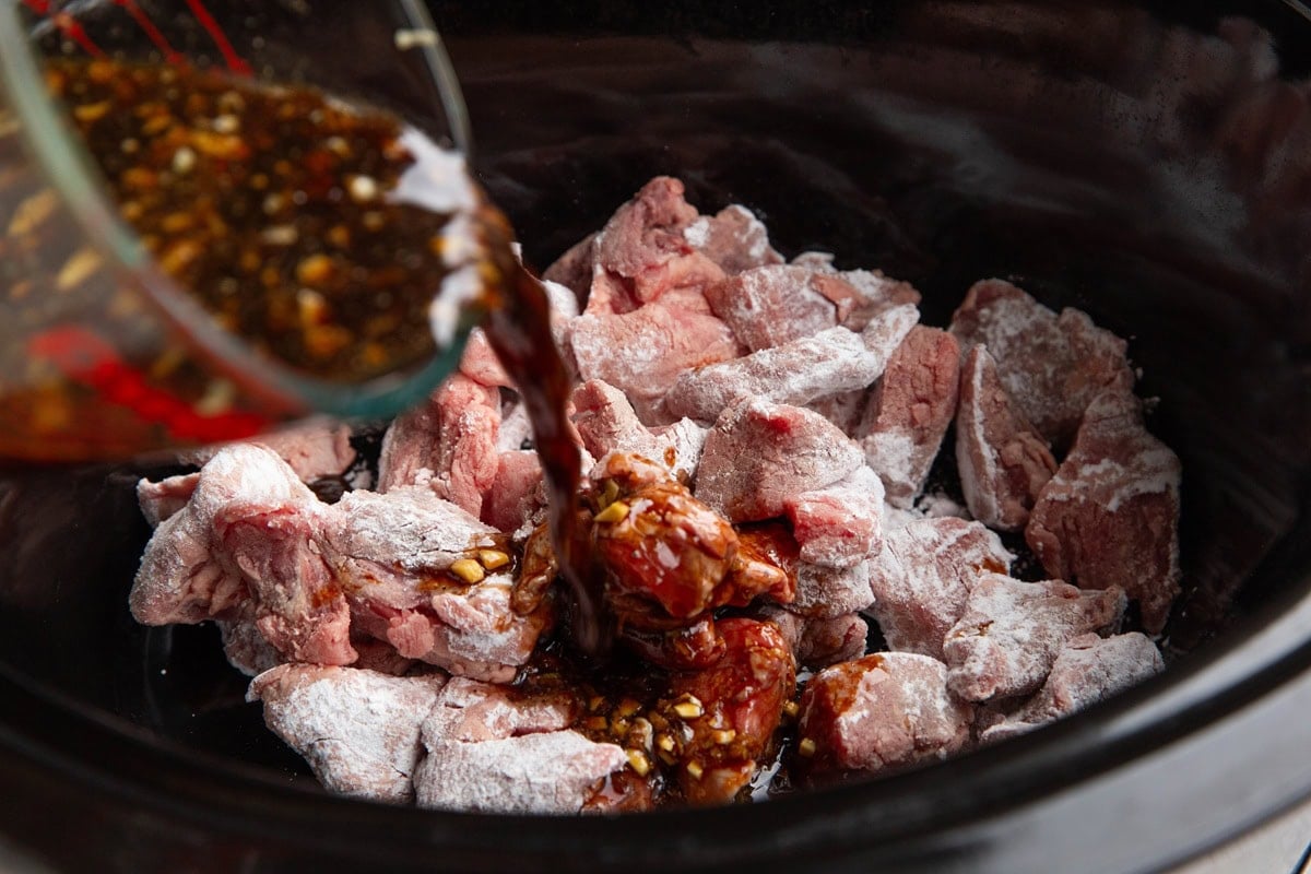 Pouring sauce into the crock pot with beef.