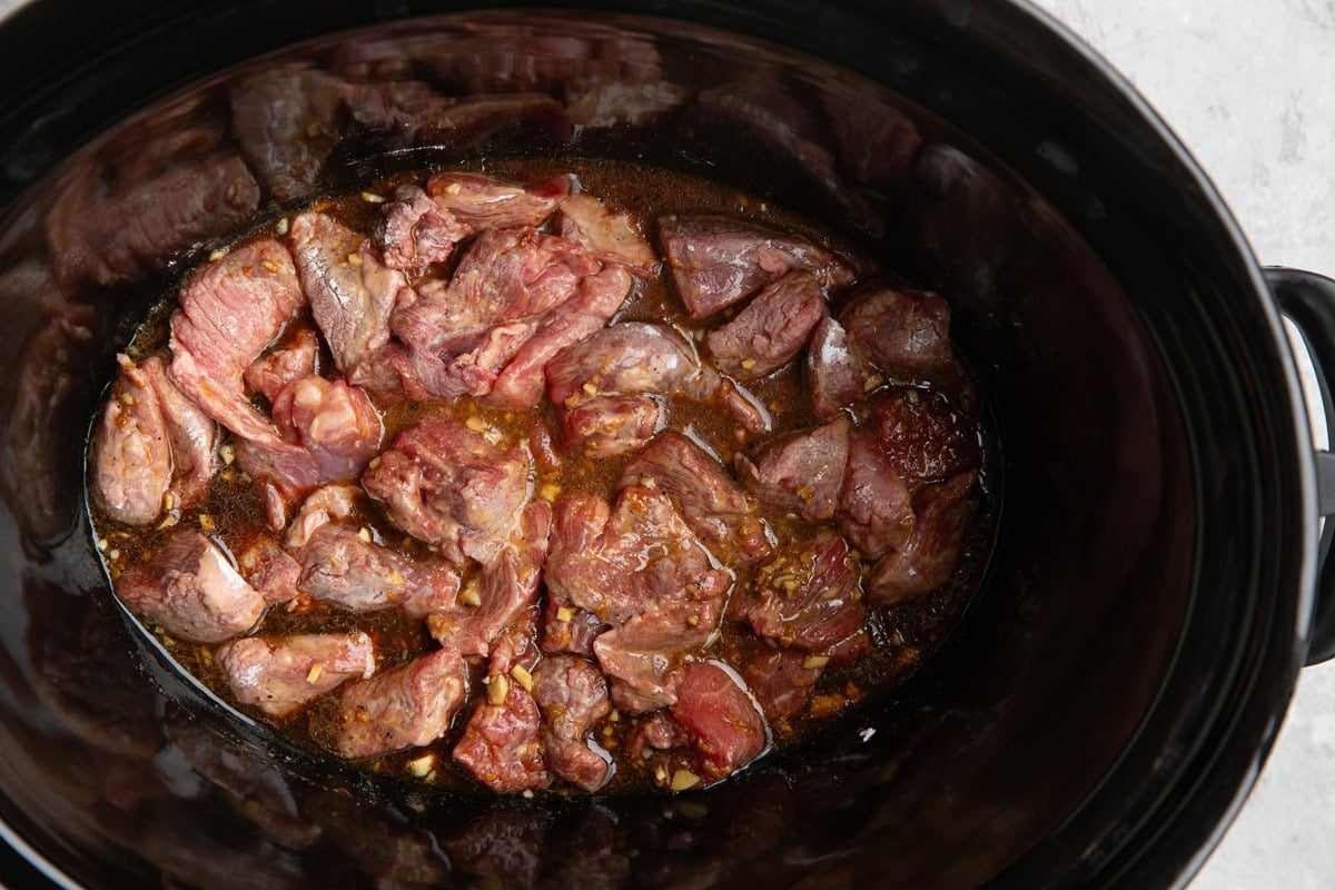 Slow cooker with chunks of beef surrounded by sauce.
