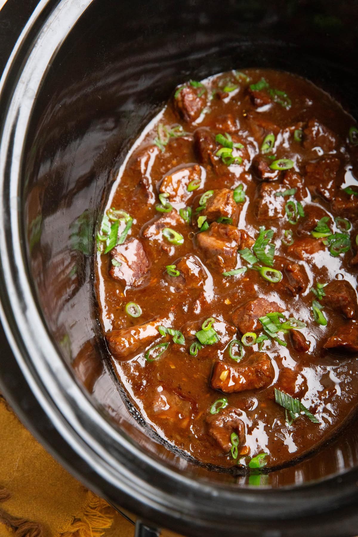 Crock pot full of Mongolian beef sprinkled with with green onions.