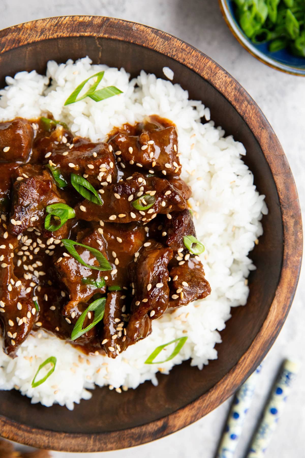 Mongolian beef in sauce on top of white rice with chop sticks to the side.