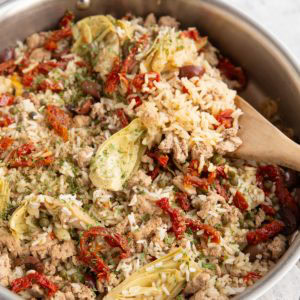Stainless steel skillet full of ground turkey, rice, and veggies with a wooden spoon scooping some of it out.