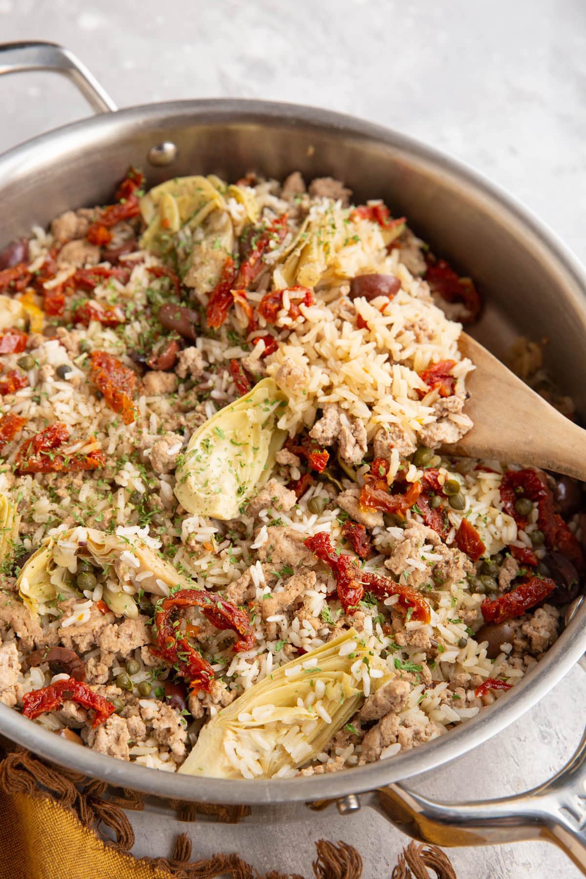 Stainless steel skillet full of ground turkey, rice, and veggies with a wooden spoon scooping some of it out.