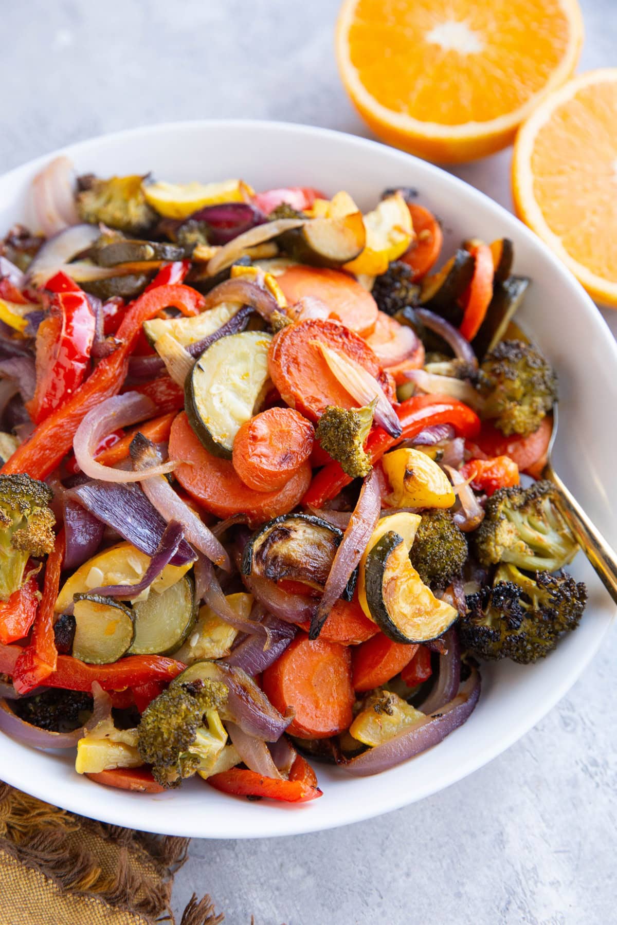 Bowl of roasted veggies in a bowl with an orange sliced in half.