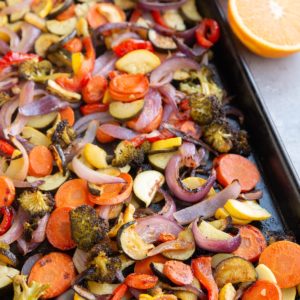 Baking sheet of roasted vegetables with an orange sliced in half.