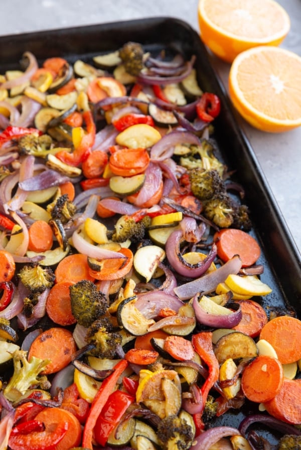 Baking sheet of roasted vegetables with an orange sliced in half.