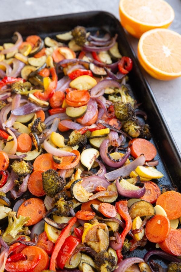 Baking sheet of roasted vegetables with an orange sliced in half.