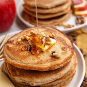 Stack of apple pancakes with butter and chopped pecans on top being drizzled with honey.