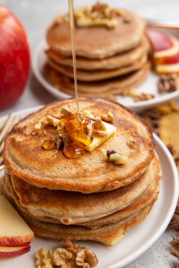 Stack of apple pancakes with butter and chopped pecans on top being drizzled with honey.