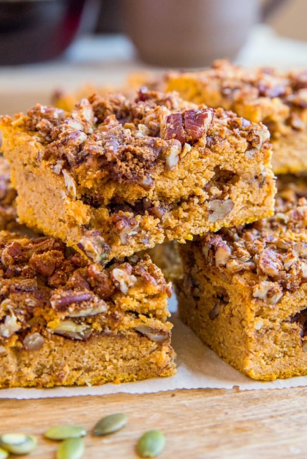 Slices of Pumpkin Coffee Cake stacked on a wooden cutting board with pumpkin seeds sprinkled around.