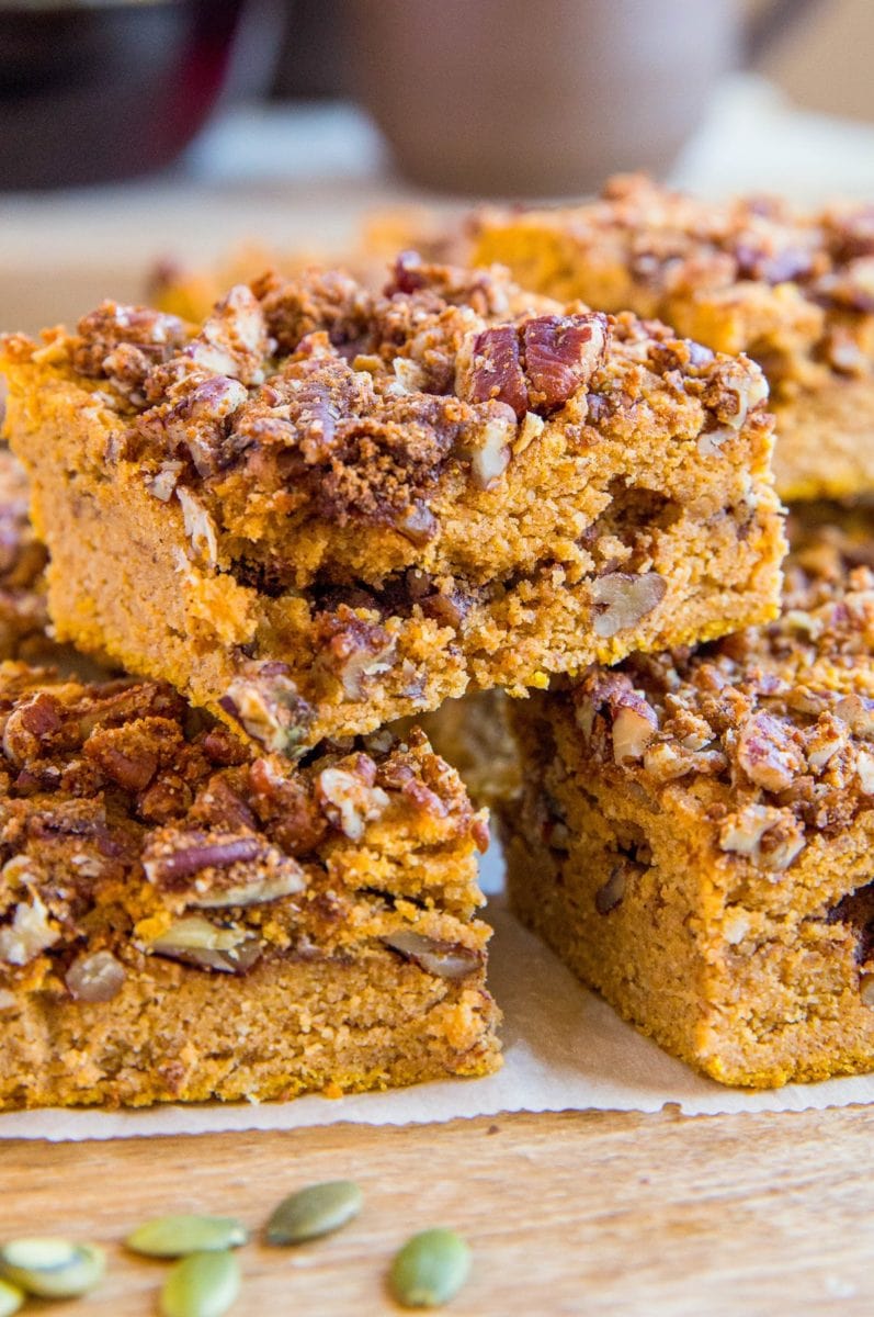 Slices of Pumpkin Coffee Cake stacked on a wooden cutting board with pumpkin seeds sprinkled around.
