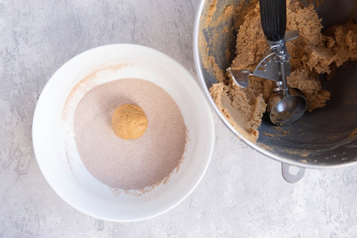 Bowl with cinnamon and sugar mixture with a ball of cookie dough to be rolled. Mixer bowl to the right with the rest of the cookie dough.