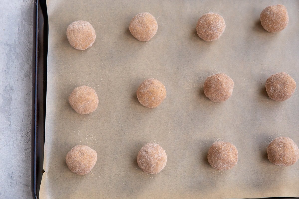 Dough balls rolled in sugar on a baking sheet lined with parchment paper.