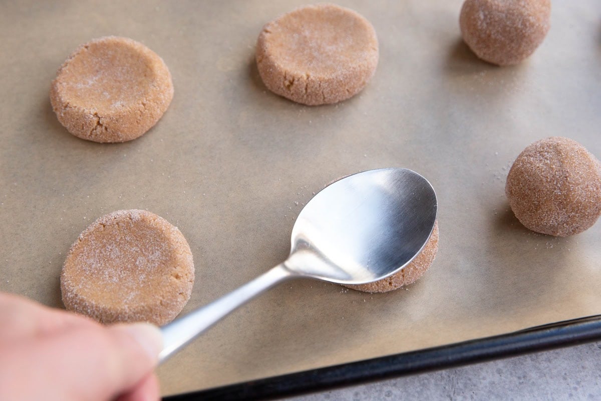 Spoon smashing the dough balls into disc shapes.