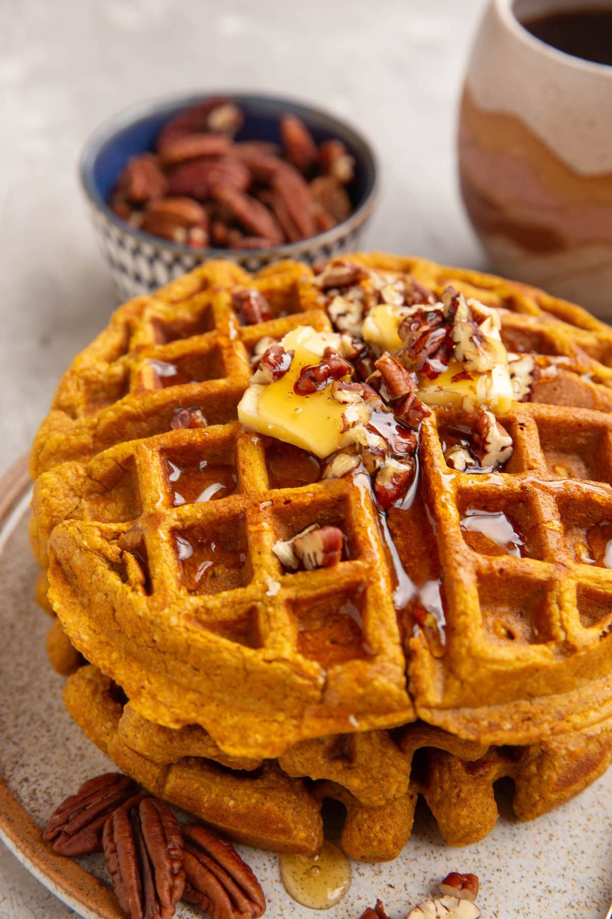 Stack of three pumpkin waffles on a plate with butter and pecans on top.