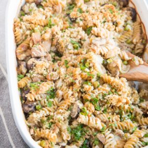 Large casserole dish full of salmon noodle casserole with a wooden spoon taking a scoop out.