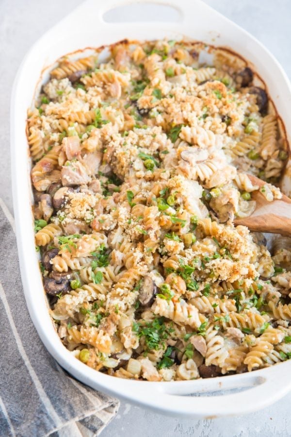 Large casserole dish full of salmon noodle casserole with a wooden spoon taking a scoop out.