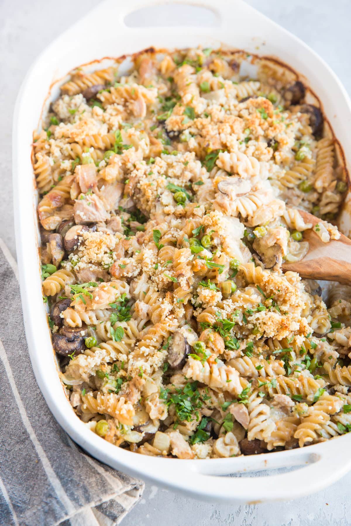 Large casserole dish full of salmon noodle casserole with a wooden spoon taking a scoop out.