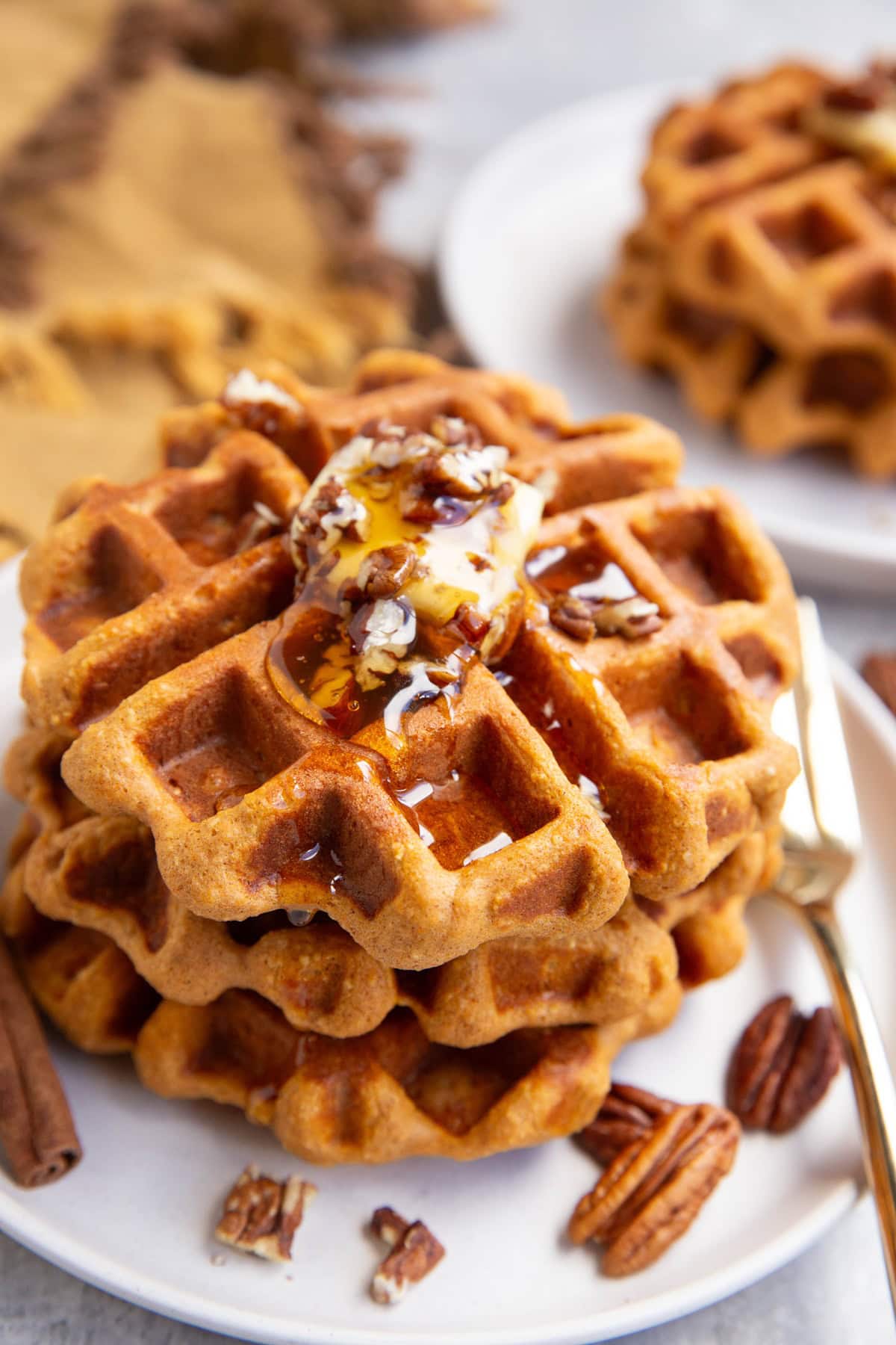 Three pumpkin waffles on a white plate with butter and chopped pecans on top, drizzled with honey with a gold fork to the side.