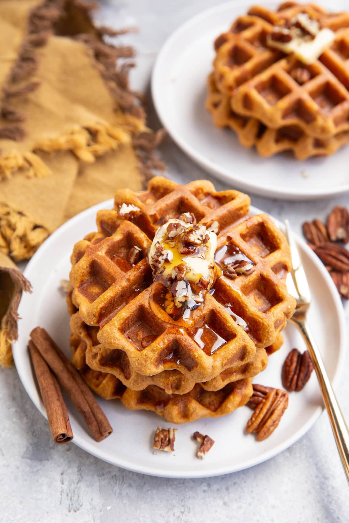 Two plates of sweet potato waffles with butter and chopped pecans on top, ready to serve.
