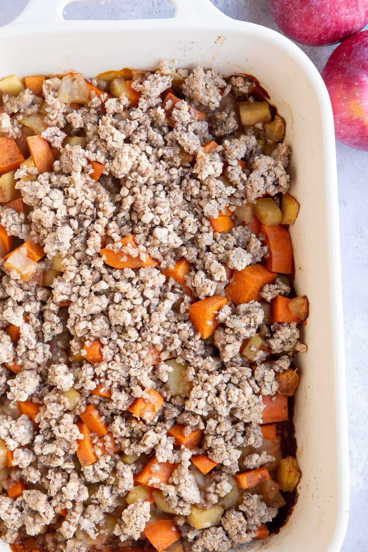 Large white casserole dish full of chopped sweet potatoes and apples, topped with a crumble topping. Ready to serve.