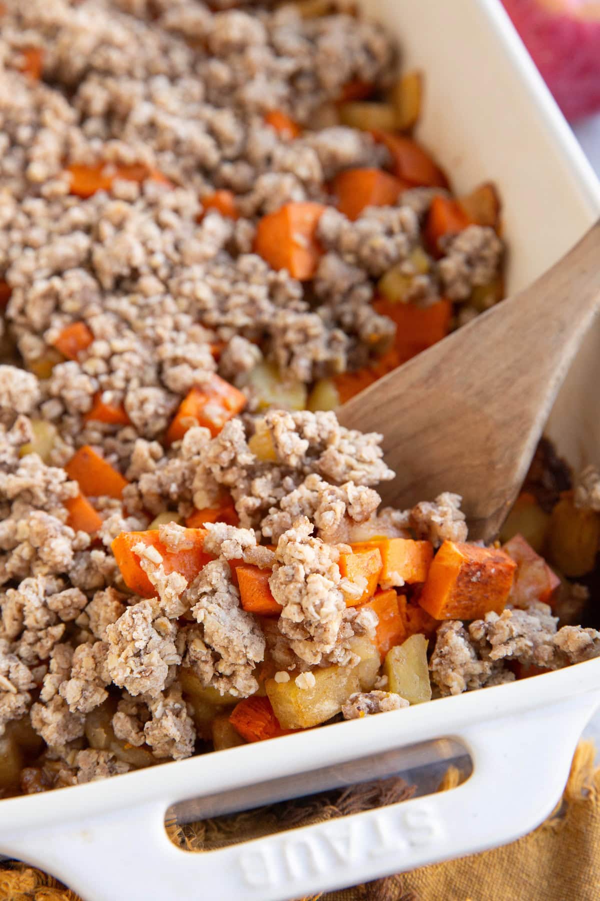 Sweet potato and apple casserole in a large white baking dish with a wooden spoon scooping some of it out.