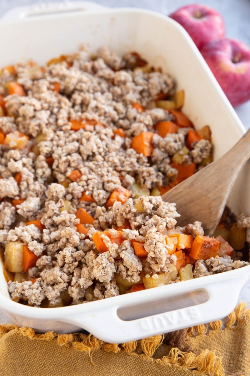 Casserole dish of sweet potato apple casserole with a wooden spoon inside the casserole, ready to serve.
