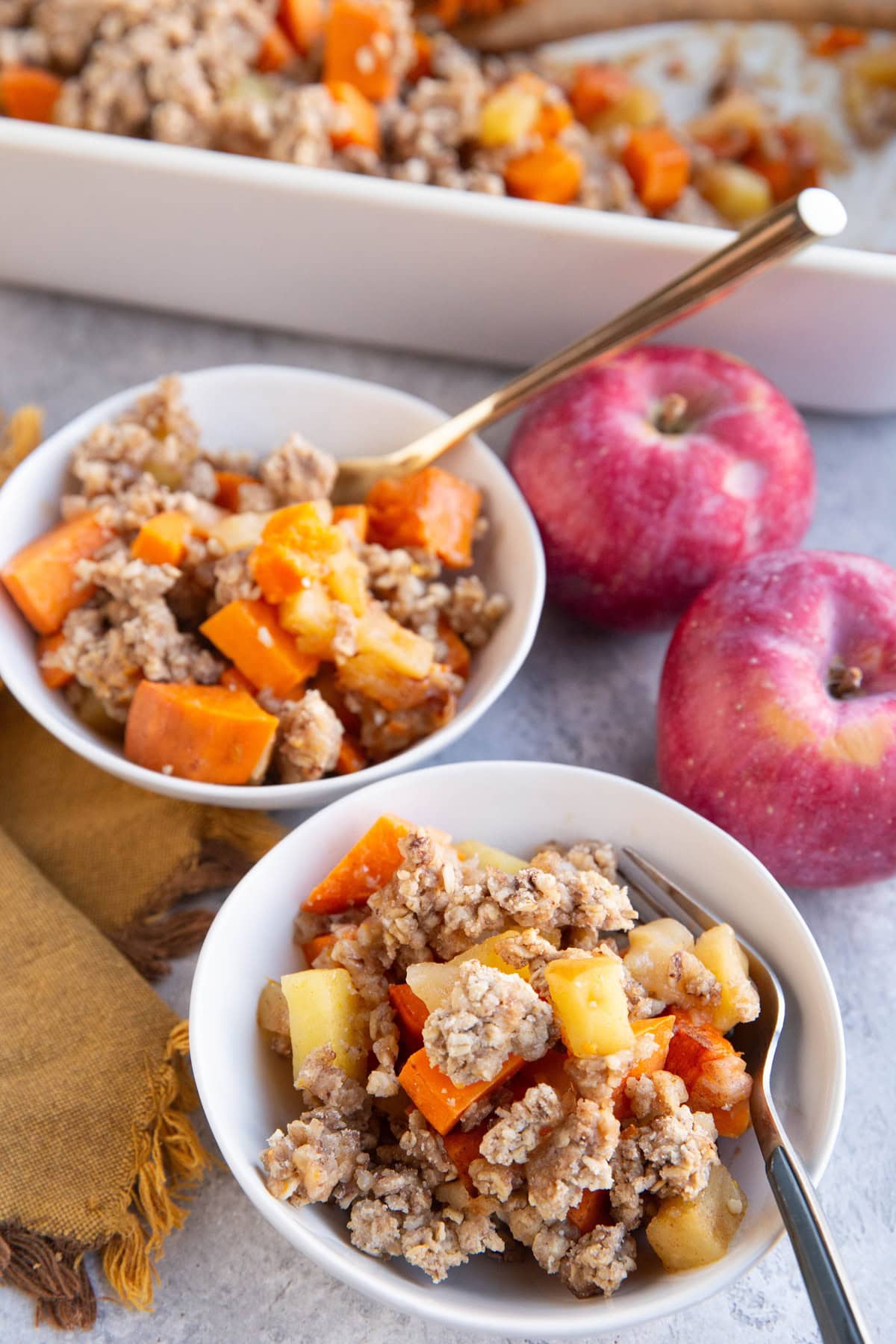 Two bowls of apple sweet potato casserole with fresh apples to the side.