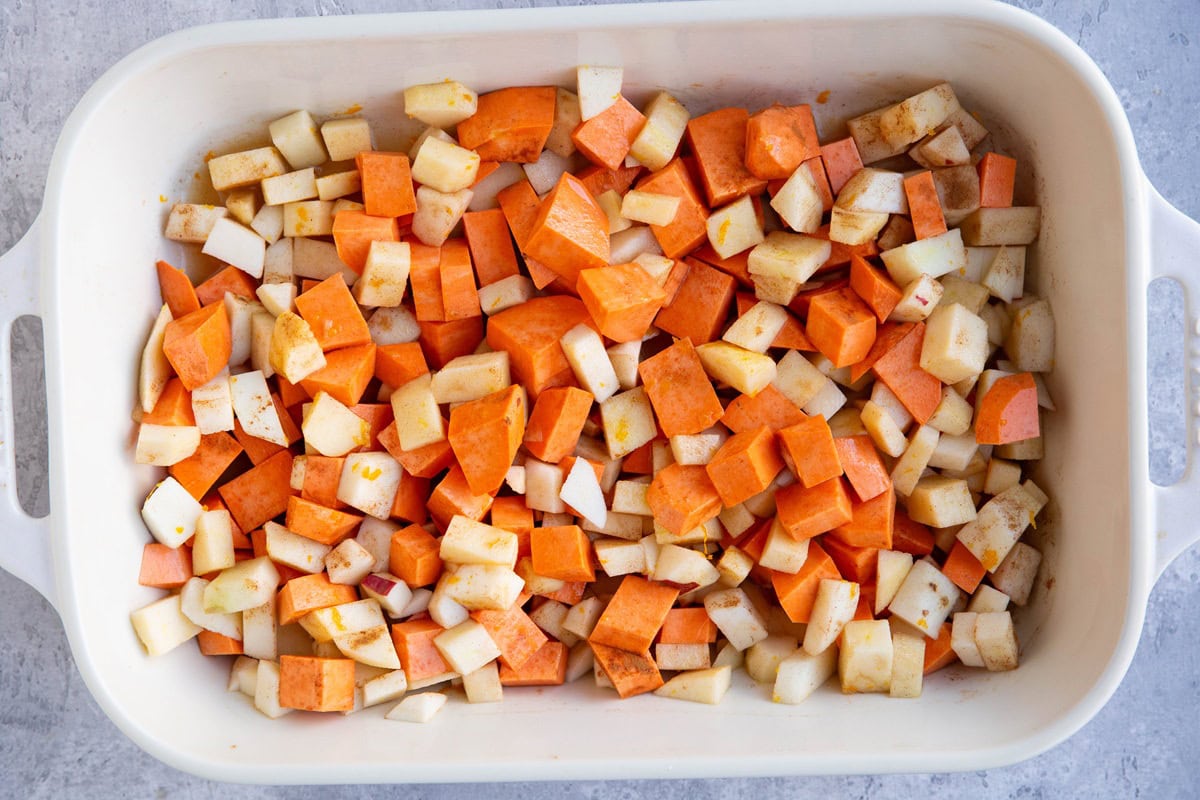 Casserole dish with chopped sweet potatoes and apples tossed in apple cider, flour, and maple syrup.