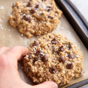 Hand picking up a tahini cookie off of a baking sheet.
