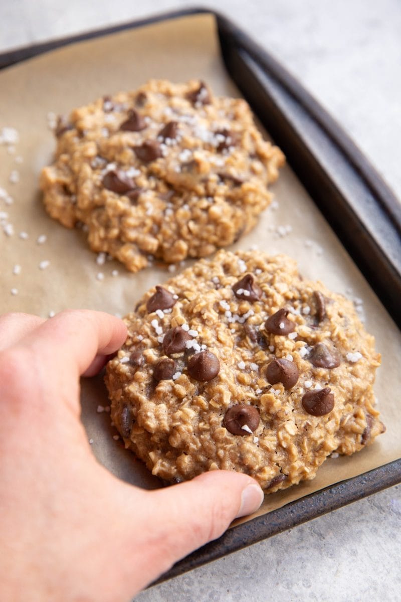 Hand picking up a tahini cookie off of a baking sheet.