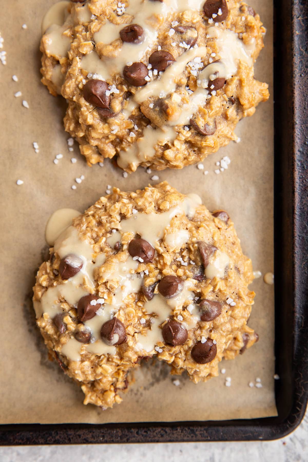 Baking sheet of tahini cookies that are drizzled with tahini and sprinkled with sea salt.