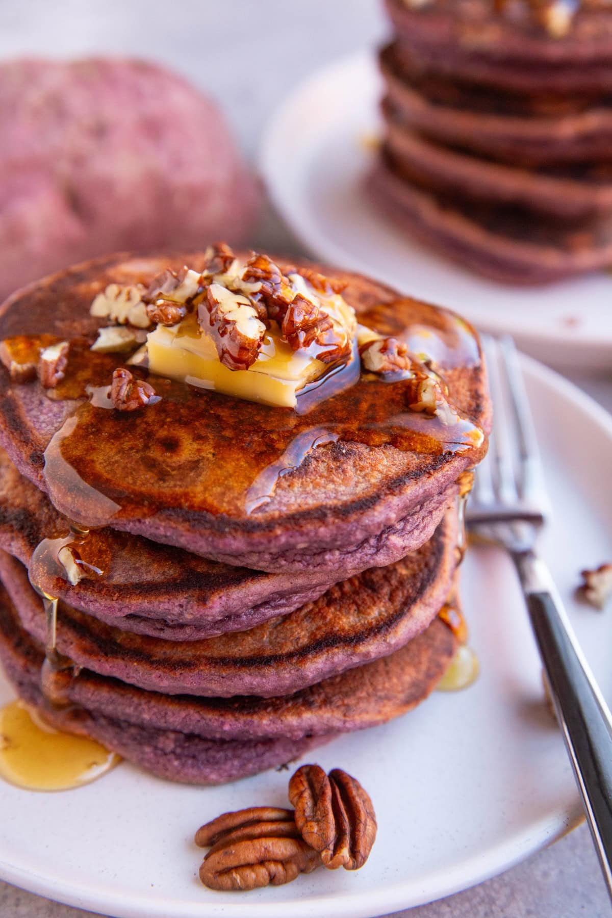 White plate of purple pancakes with butter, chopped nuts, and honey on top, ready to serve.