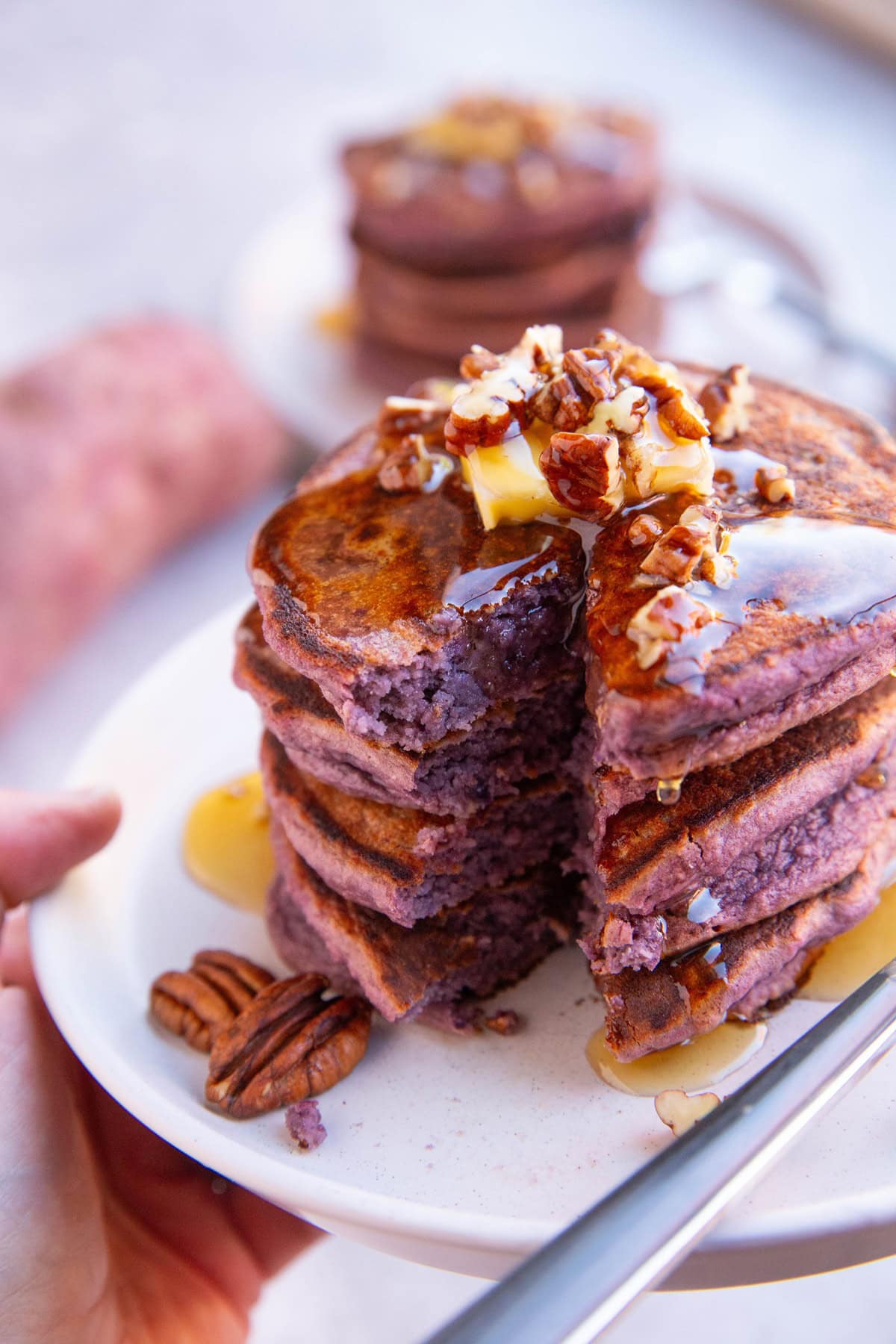 hand holding a plate of purple sweet potato pancakes with a bite taken out.