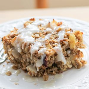 Thick slice of apple baked oatmeal sitting on a plate, drizzled with a glaze. Ready to eat.